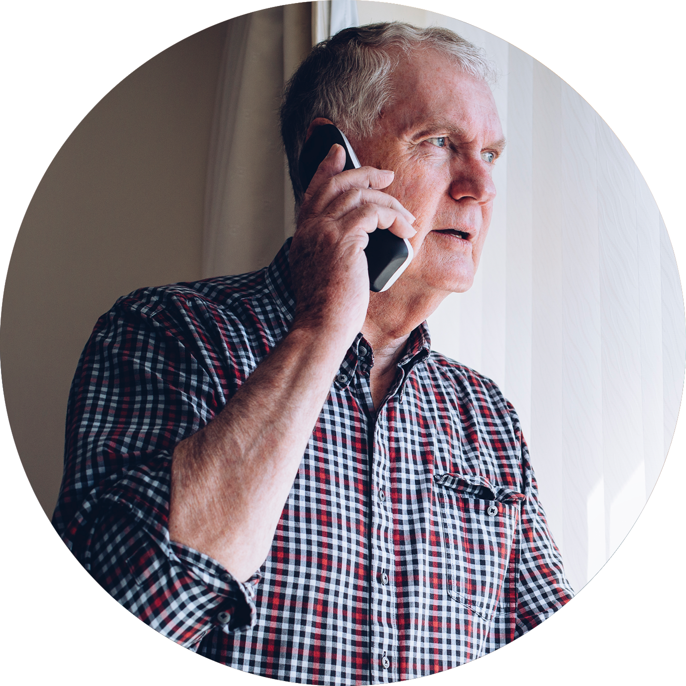 An older man talks on the phone while looking out of the window