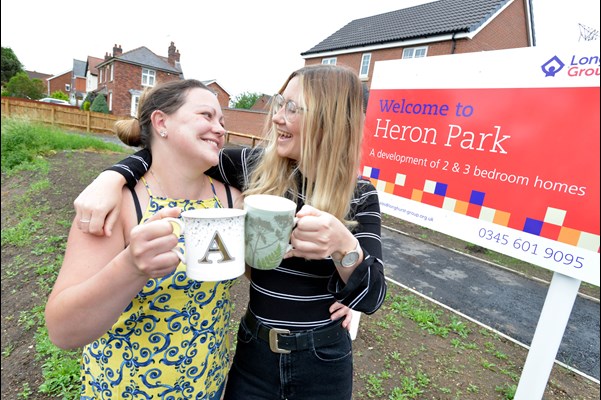 Two ladies holding a mug outside Heron Park sign