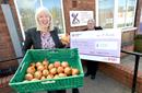 One lady holding a cheque, another lady holding a basket of onions