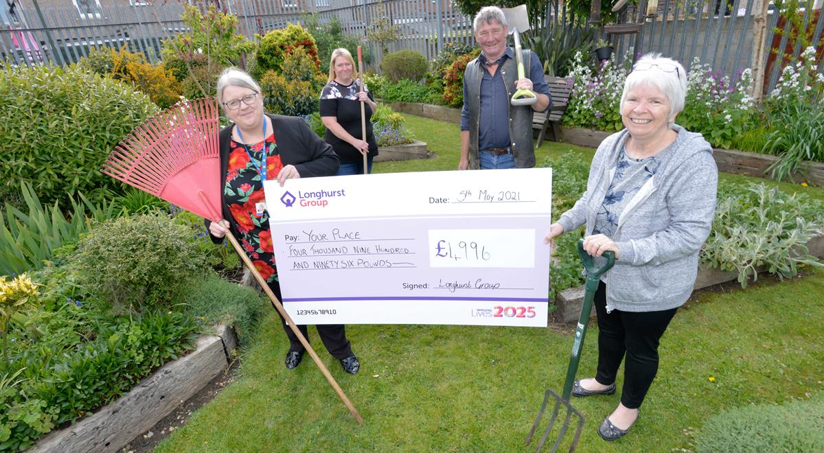 A group of people in a garden holding gardening tools and a cheque