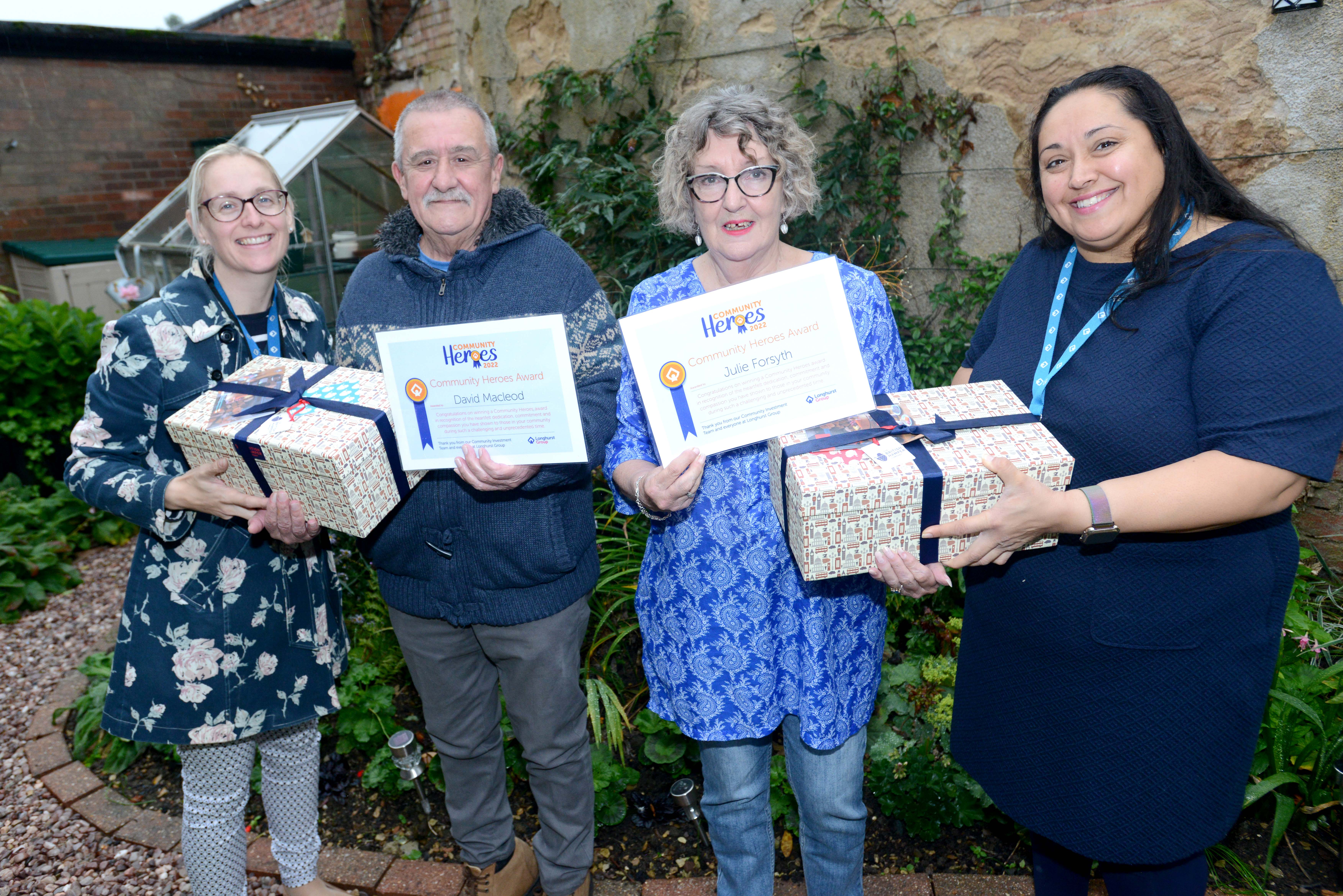 Three ladies and a man smiling holding their gifts and certificates