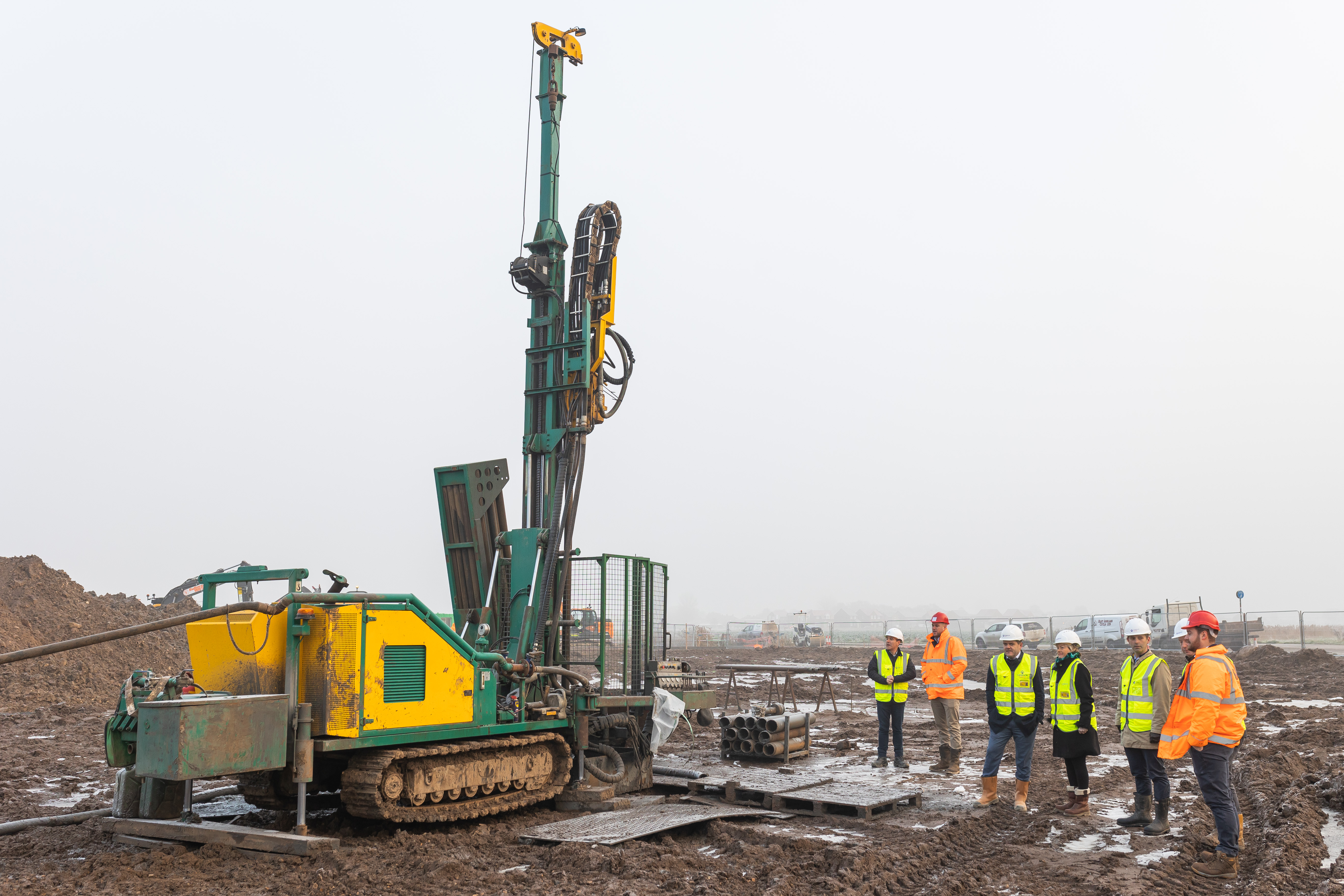 Men and women in hard hats standing on a muddy field