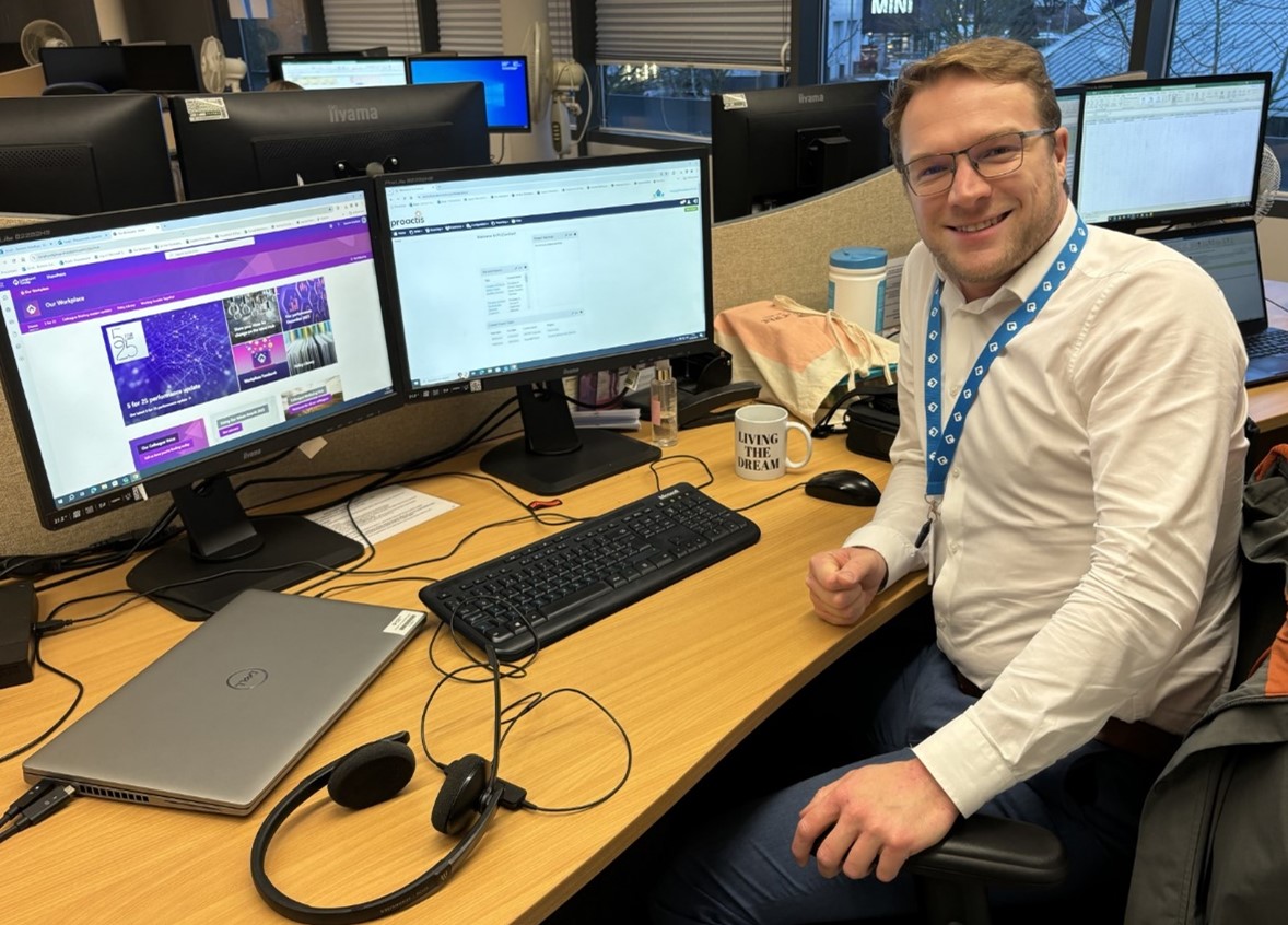 Man smiles as he works from his office desk, with a cup of tea ready to drink.